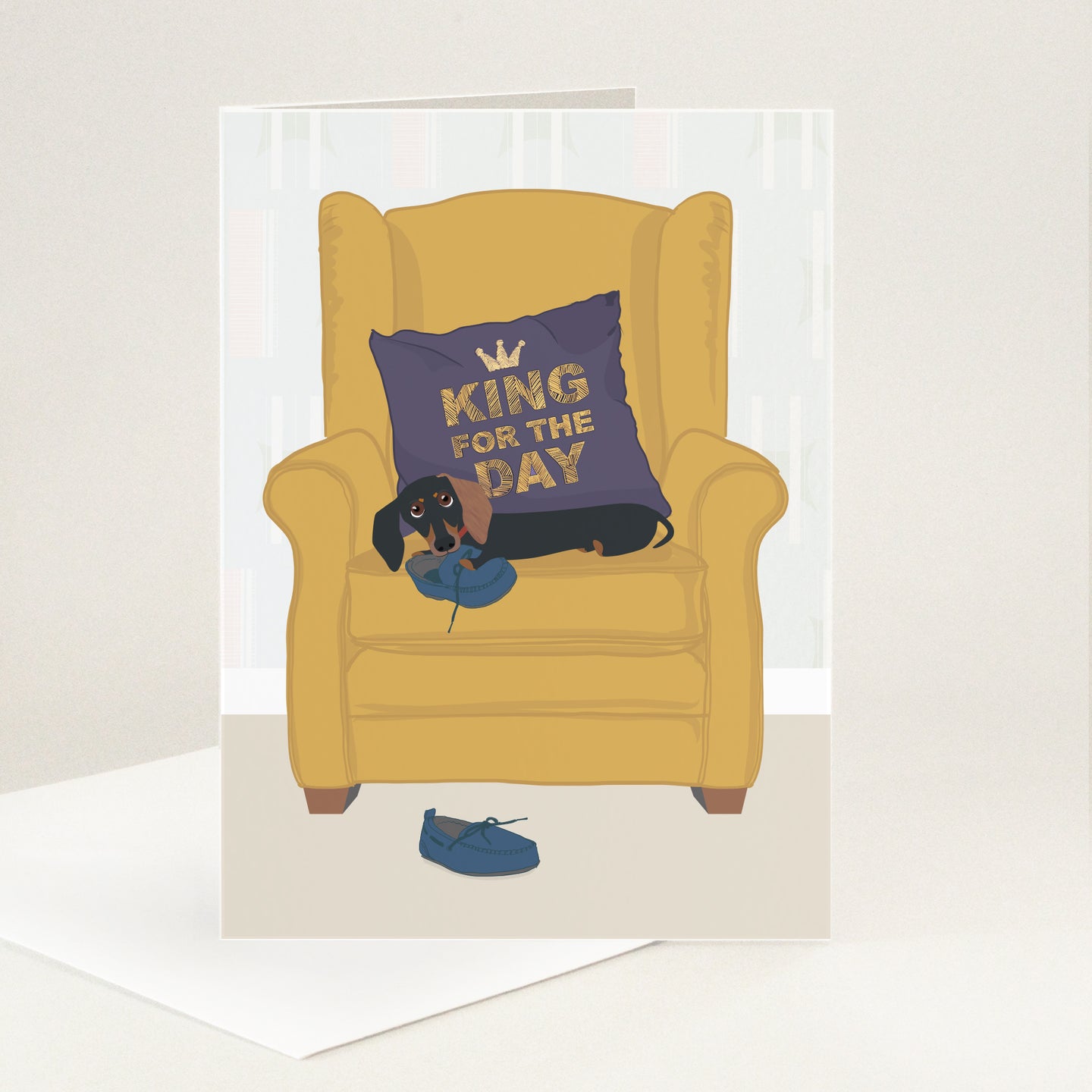 King for the Day embroidered onto a purple cushion on a gold armchair with a sausage dog laying on the chair and chewing one of a pair of blue moccasin slippers. 